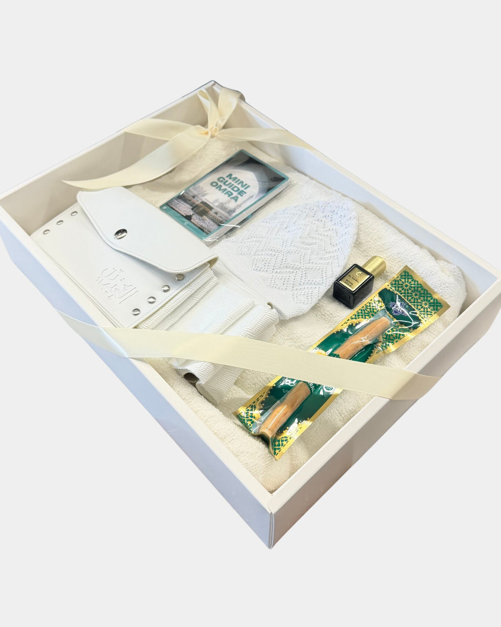 Coffret cadeau Omra et Hajj Al Rezam ouvert : ihram en coton blanc, ceinture ihram en cuir blanc et chechia blanche, présentés dans une boîte blanche nouée d'un ruban ivoire