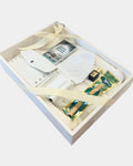 Coffret cadeau Omra et Hajj Al Rezam ouvert : ihram en coton blanc, ceinture ihram en cuir blanc et chechia blanche, présentés dans une boîte blanche nouée d'un ruban ivoire