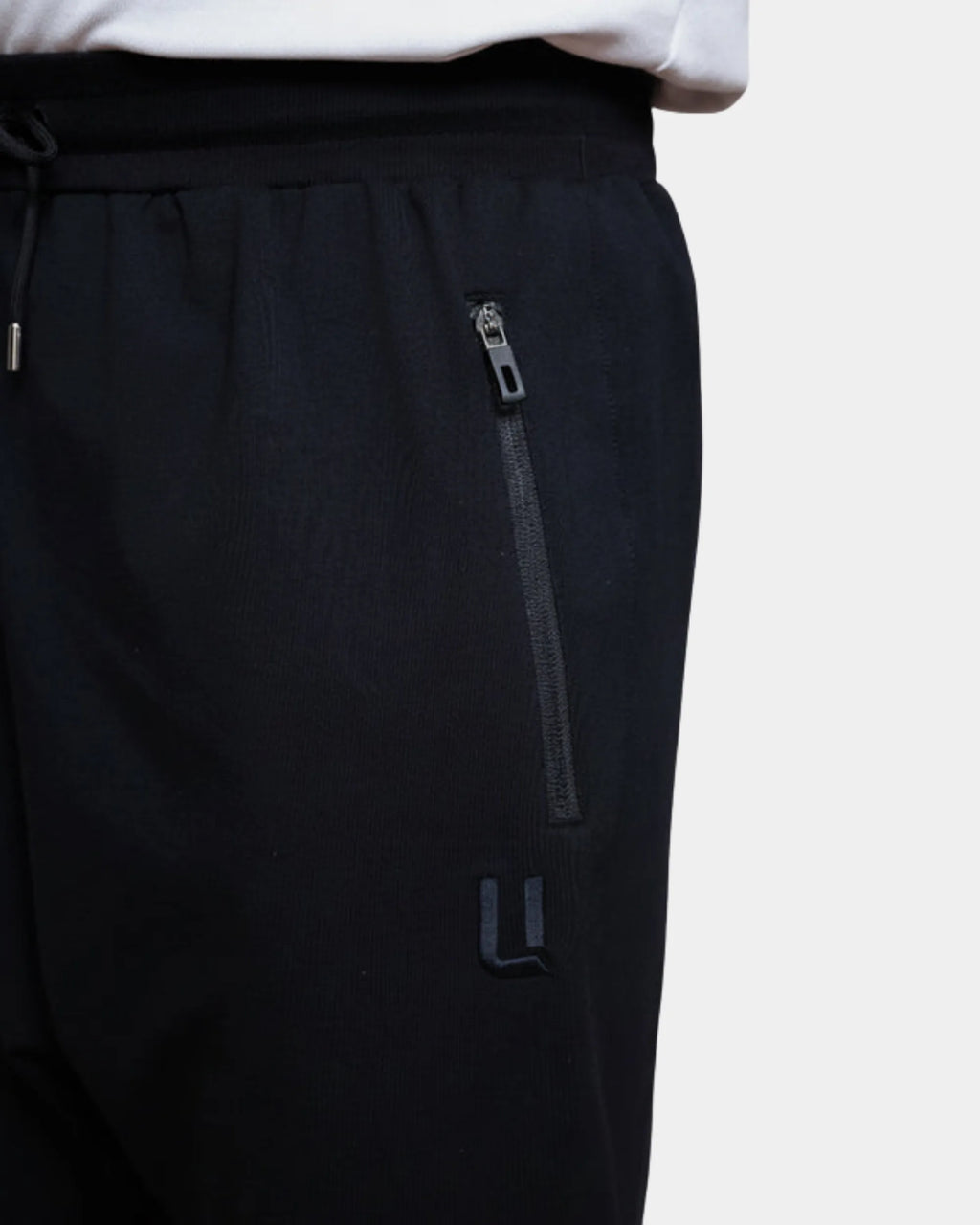 Détail poche zippée et logo brodé du jogging sarouel noir