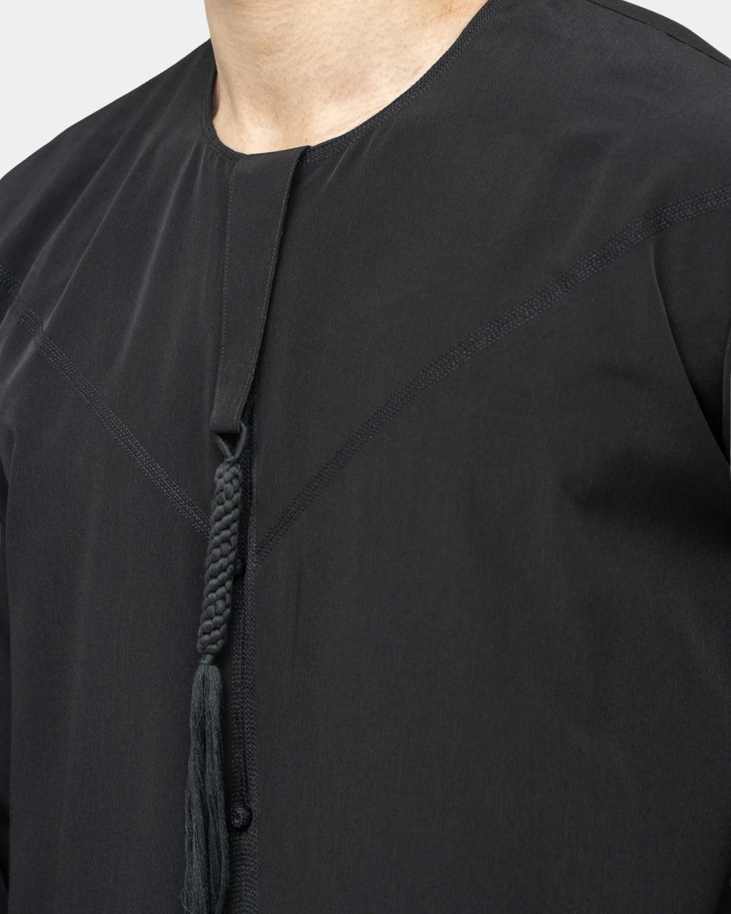 Qamis Dubaï noir Al Rezam porté de profil — coupe droite fluide et gland tarbousha au col