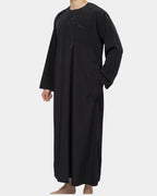 Qamis marocain noir Al Rezam porté de profil — tombé fluide, poches latérales et col rond brodé