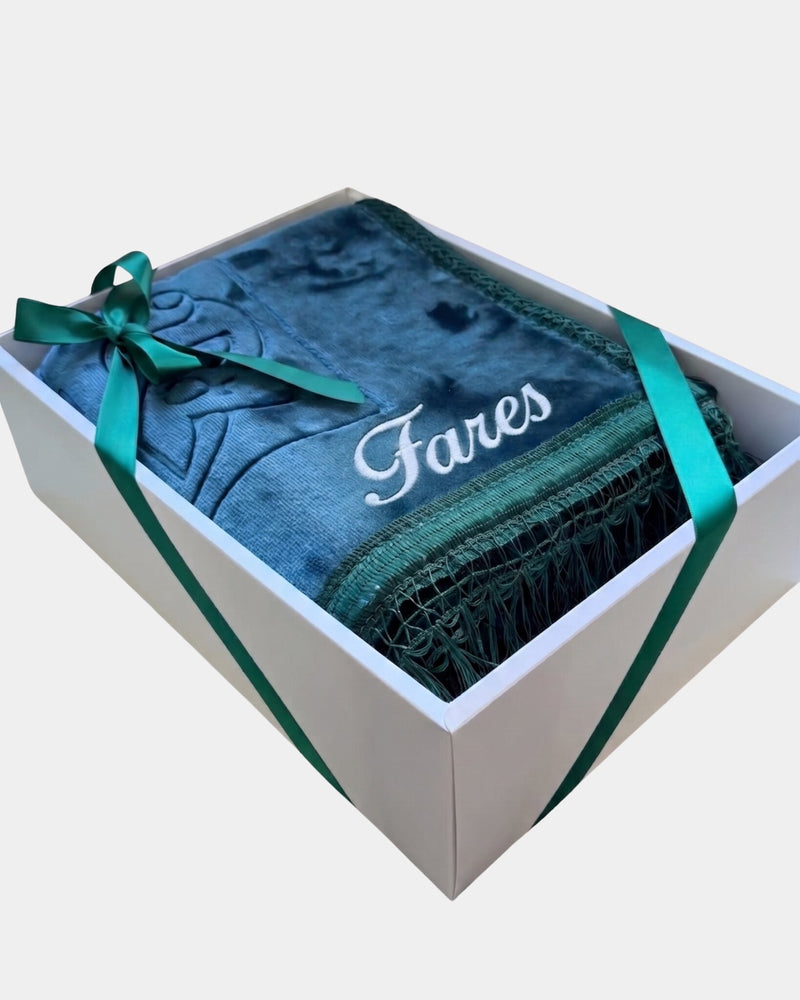 Tapis de prière épais en velours bleu canard à motif embossé avec le prénom Fares brodé en fil blanc, présenté dans un coffret cadeau blanc noué d'un ruban vert assorti