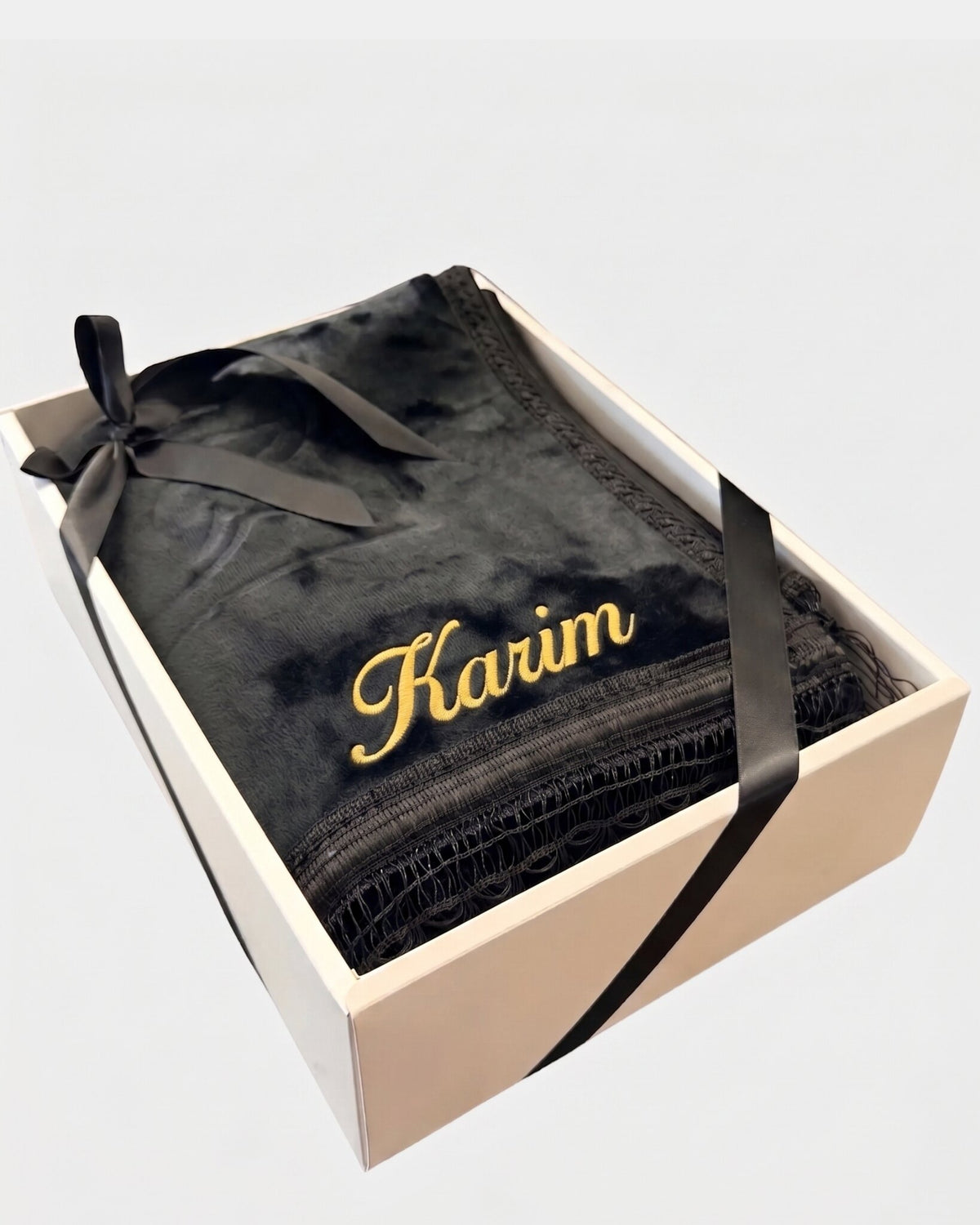 Tapis de prière épais en velours noir à motif embossé avec le prénom Karim brodé en fil doré, présenté dans un coffret cadeau blanc noué d'un ruban noir assorti