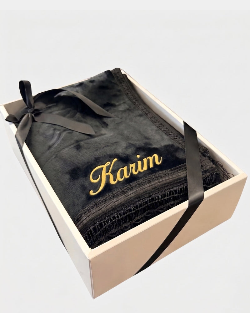 Tapis de prière épais en velours noir à motif embossé avec le prénom Karim brodé en fil doré, présenté dans un coffret cadeau blanc noué d'un ruban noir assorti