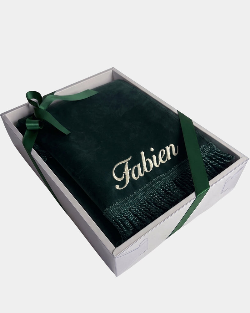 Tapis de prière en velours vert sapin avec le prénom Fabien brodé en fil ivoire, présenté dans un coffret cadeau blanc noué d'un ruban vert assorti